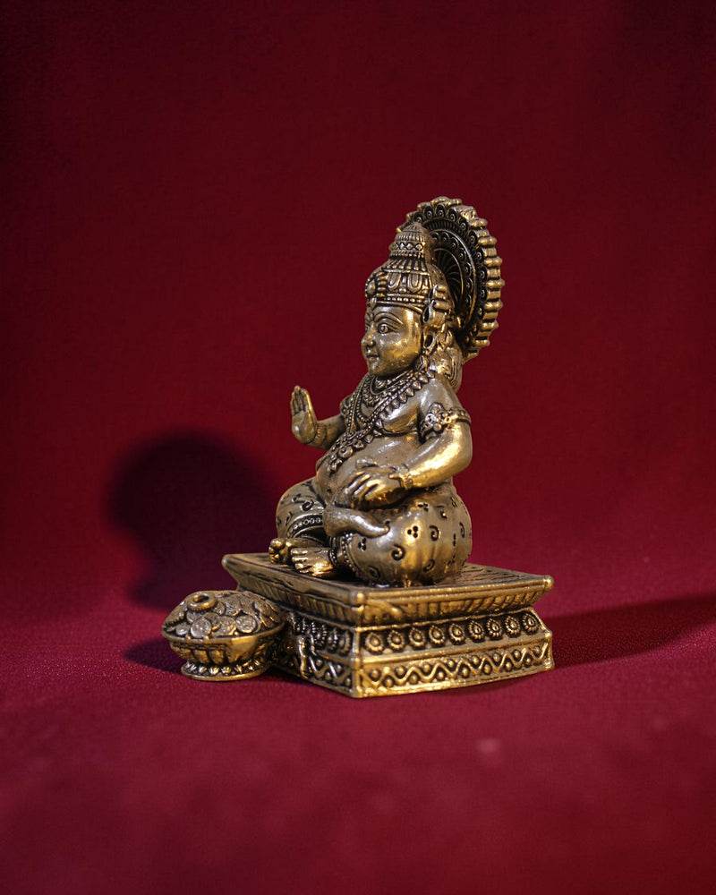 Rigvedaa	exttrademark
 brass Kuber idol sitting on a chowki, holding a money pot. Detailed ornamentation, golden patina.
