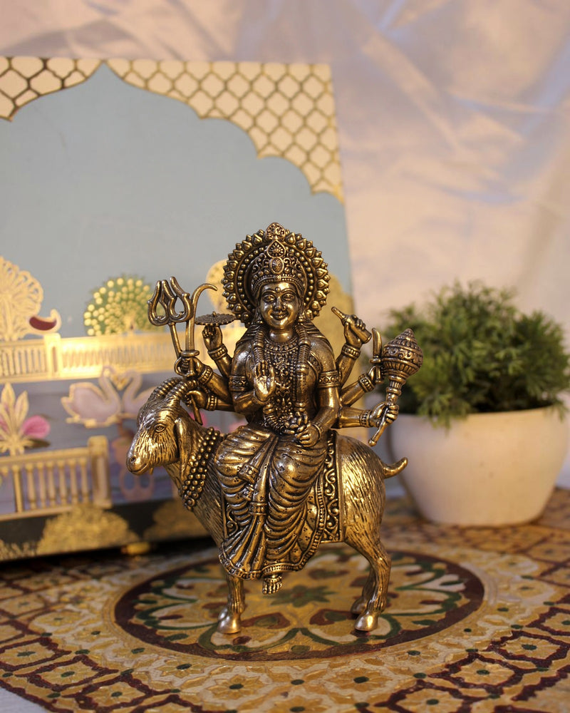 Rigvedaa™ Brass Meldi Maa statue on goat, a protective folk goddess sculpture with multiple arms holding weapons, golden patina.