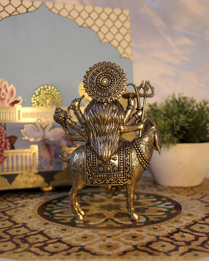 Rigvedaa Brass Meldi Maa statue on goat, protective folk goddess sculpture with multiple arms and weapons, golden patina.