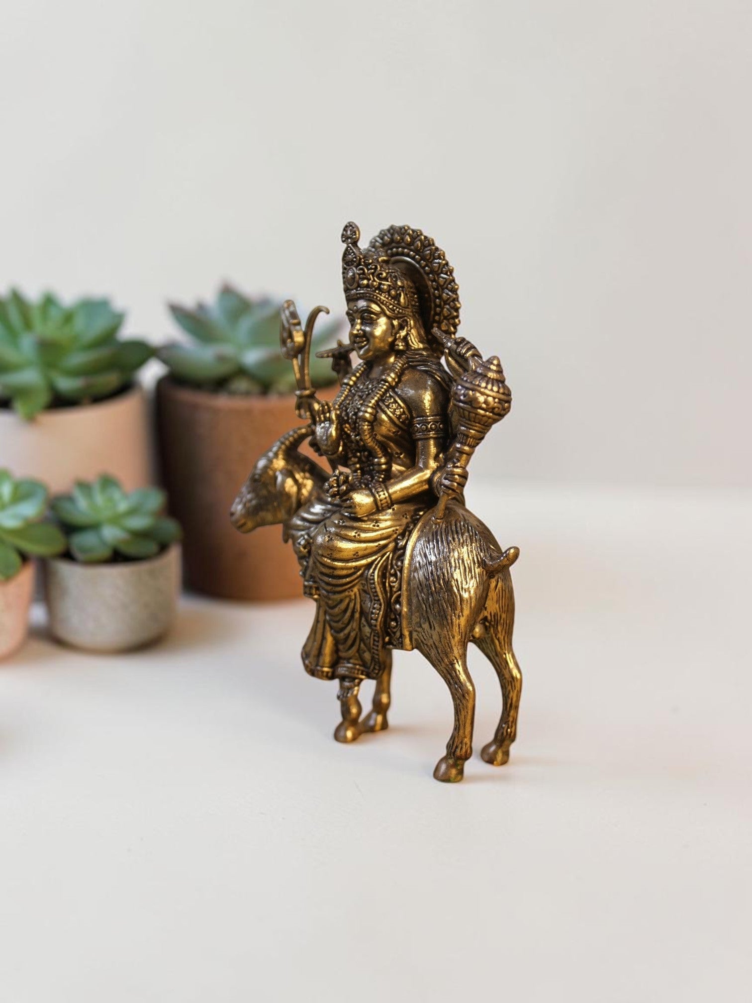 Rigvedaa™ brass Meldi Maa statue featuring the goddess seated on a goat, with intricate golden patina and weapon details.