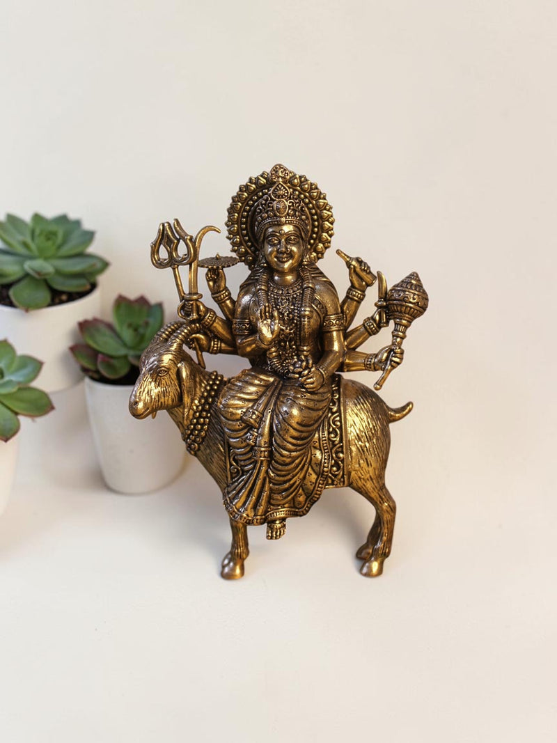 Rigvedaa™ brass Meldi Maa statue featuring the goddess seated on a goat, with intricate weapons and golden patina.