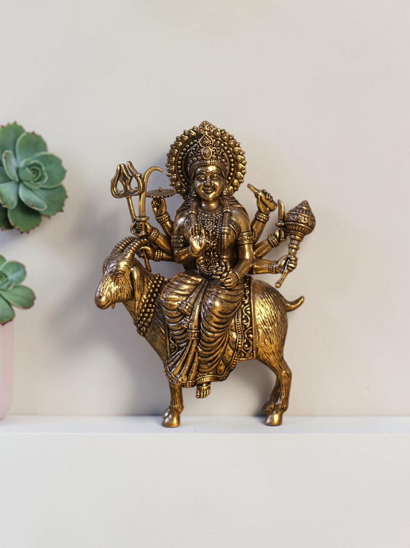 Rigvedaa™ brass Meldi Maa statue featuring the goddess seated on a goat, with intricate golden patina and weapon details.