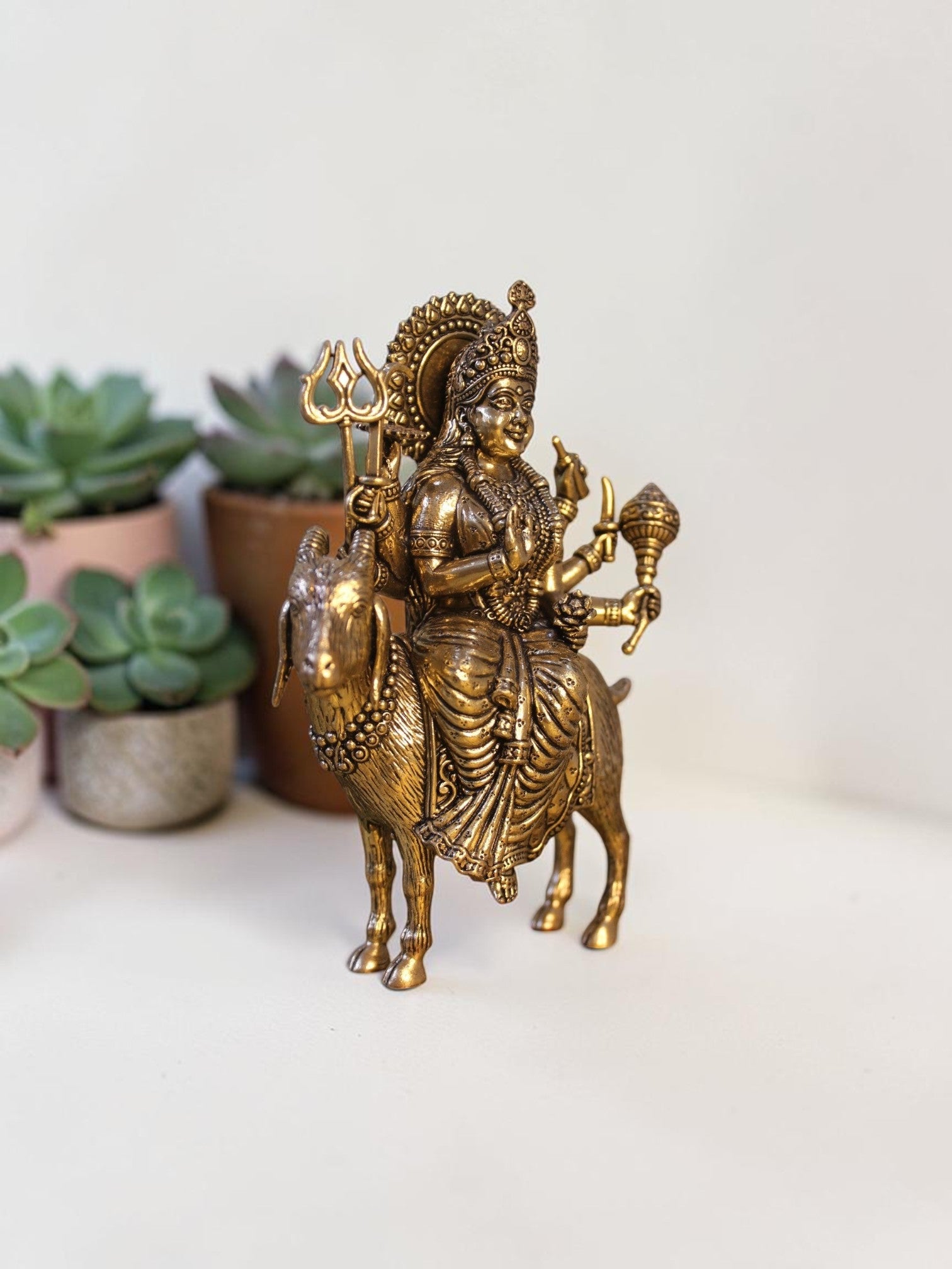 Rigvedaa™ brass Meldi Maa statue featuring the goddess seated on a goat, with intricate golden patina detailing.