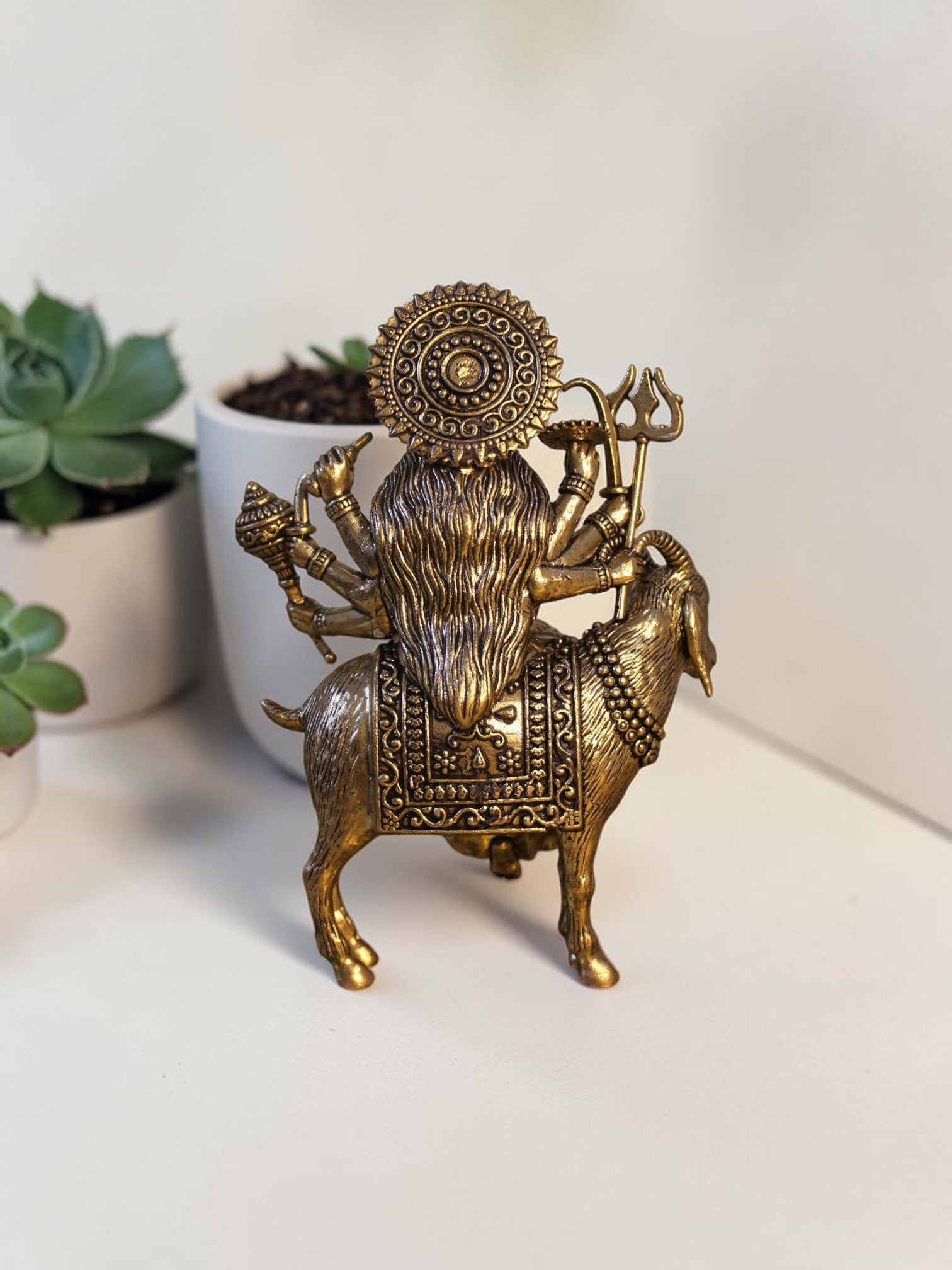 Rigvedaa™ brass Meldi Maa statue showing the goddess seated on a goat, featuring intricate golden patina detailing.
