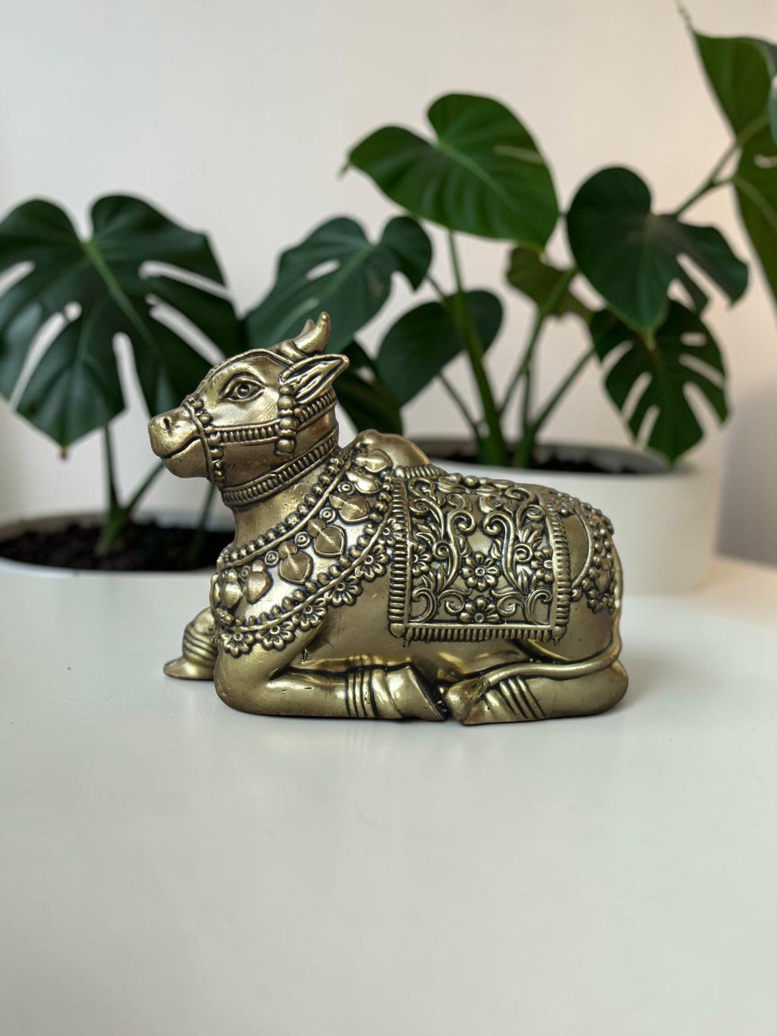 Rigvedaa™ handcrafted brass Nandi idol featuring intricate floral engravings and beadwork on a white table.