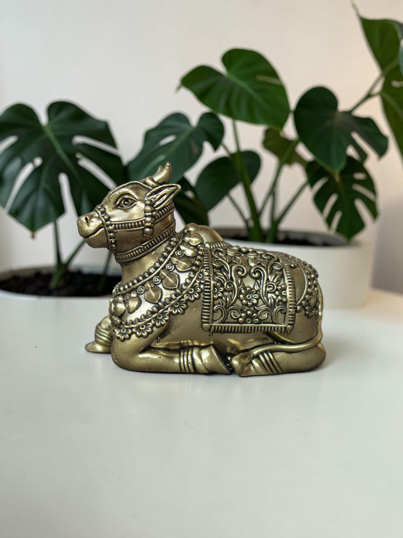 Rigvedaa™ handcrafted brass Nandi idol featuring intricate floral engravings and beadwork on a white table.