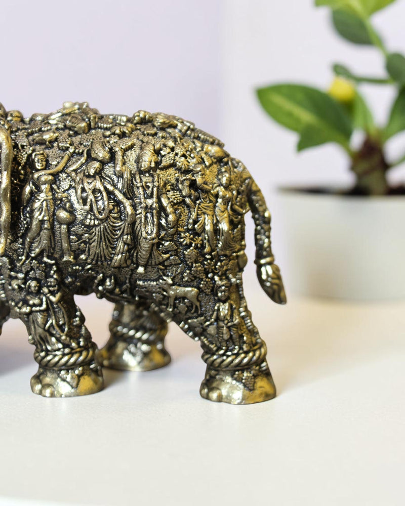 Rigvedaa™ brass elephant statue featuring intricate hand-carved Radha Krishna murals and a golden antique finish.
