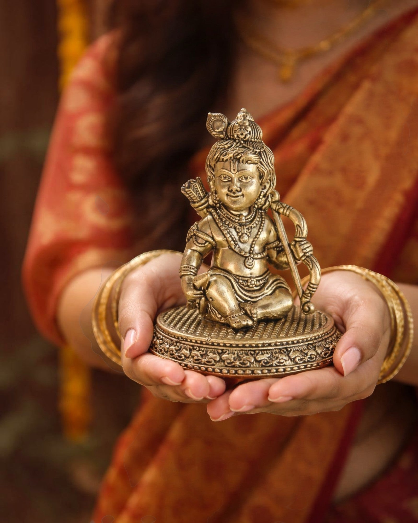 Rigvedaa

Brass Ram Lalla idol, 4-inch, seated child form of Lord Ram with bow and arrow, intricate details, golden patina, held in hands.