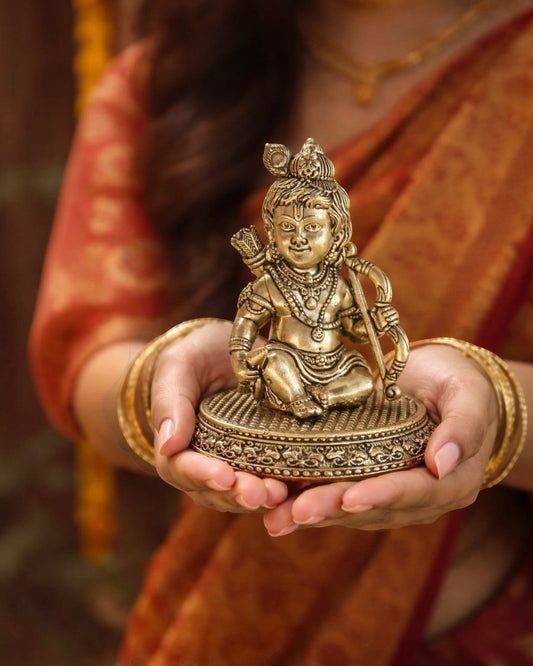 Rigvedaa

Brass Ram Lalla idol, 4-inch, seated child form of Lord Ram with bow and arrow, intricate details, golden patina, held in hands.