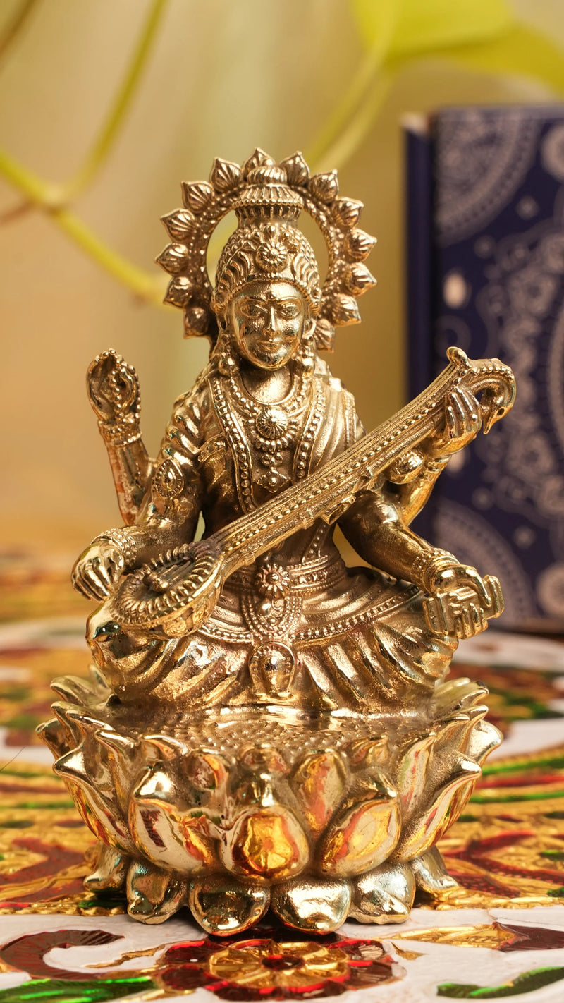 Rigvedaa™ brass Saraswati idol seated on lotus, holding veena and scriptures. Symbolizes knowledge and creativity.