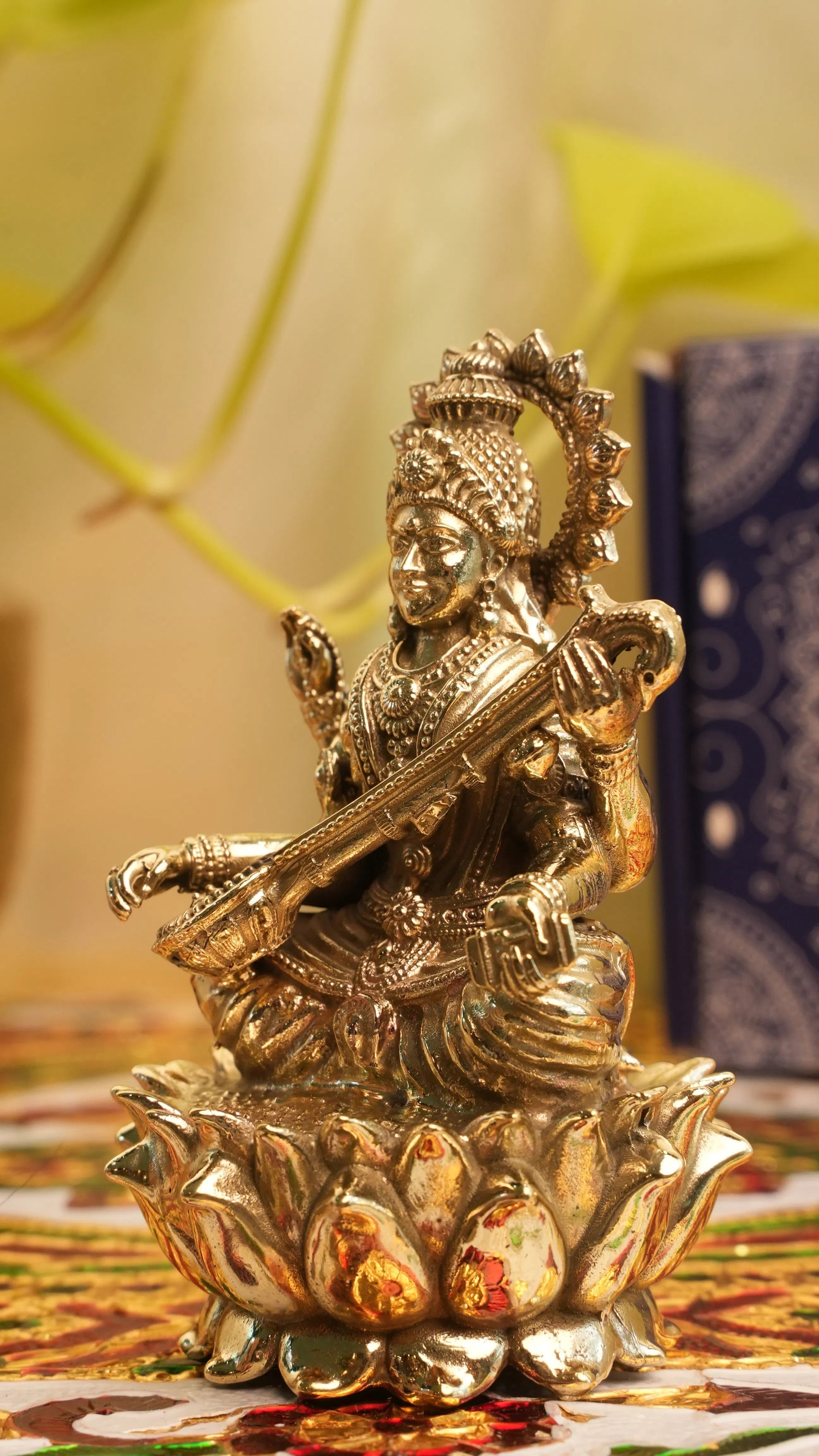Rigvedaa™ brass Saraswati idol seated on lotus, holding veena and scriptures. Detailed, golden finish, divine sculpture.