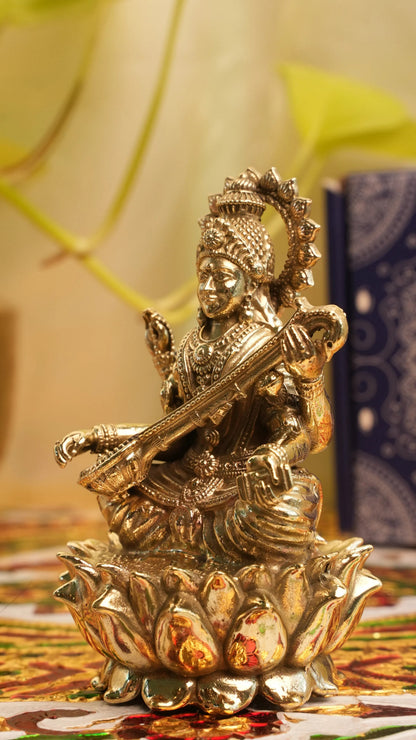 Rigvedaa™ brass Saraswati idol seated on lotus, holding veena and scriptures. Detailed, golden finish, divine sculpture.