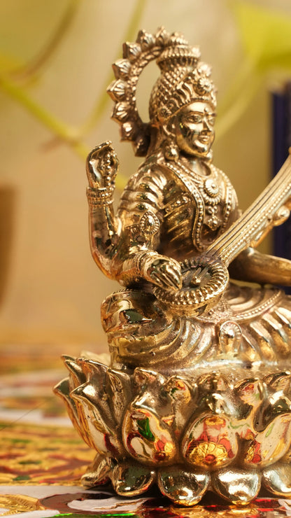 Rigvedaa™ brass Saraswati idol seated on a lotus, holding a veena and scriptures. Detailed, golden finish.