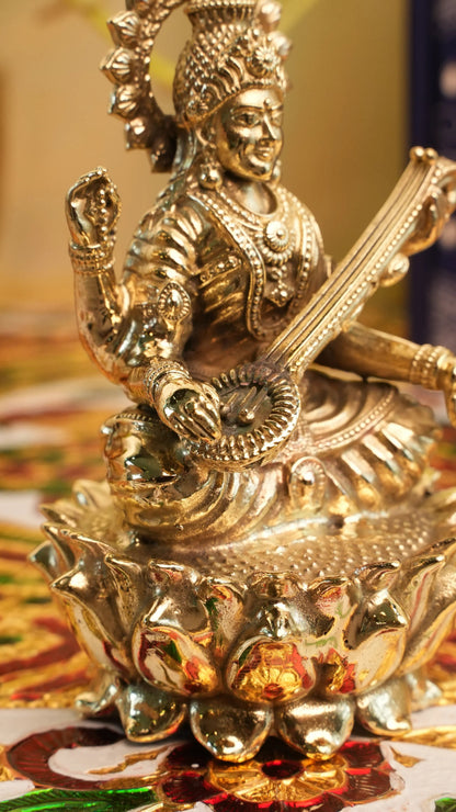Rigvedaa™ brass Saraswati idol seated on a lotus, holding a veena and scriptures. Detailed, golden finish.
