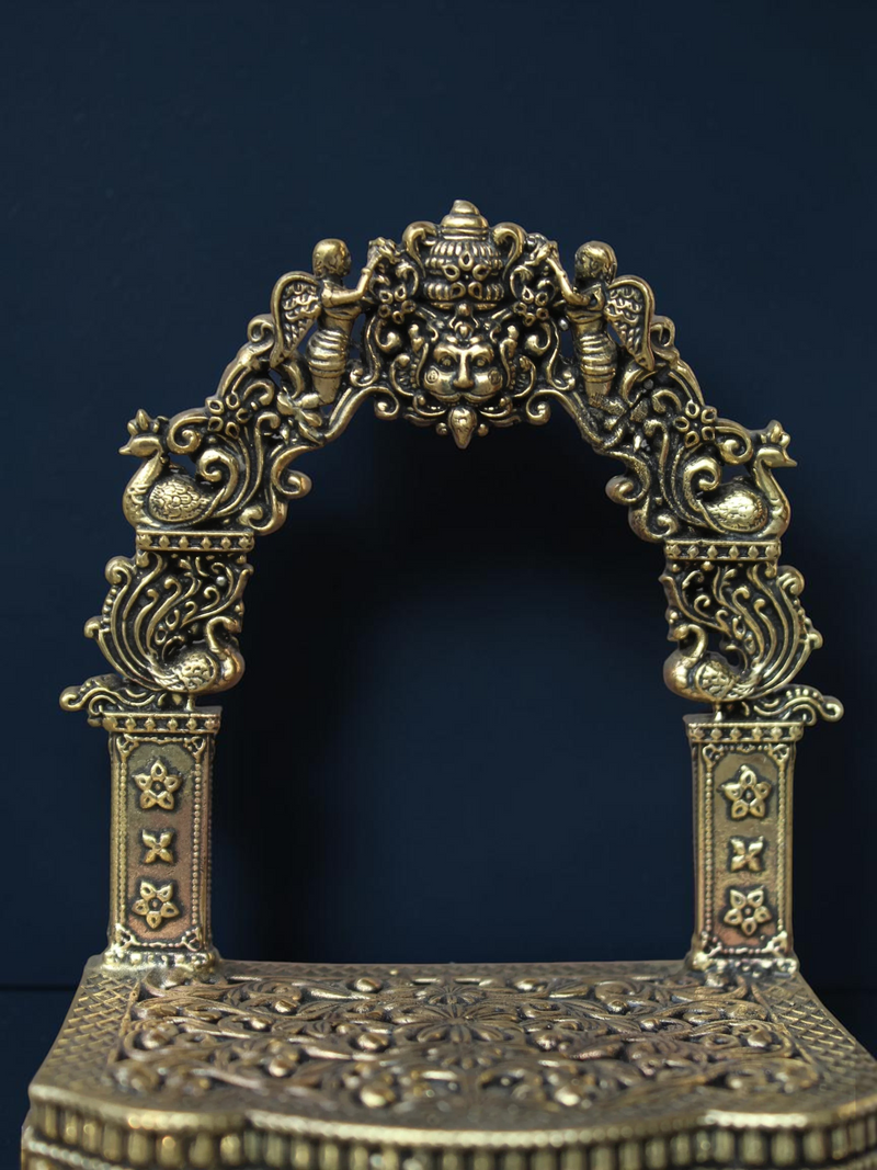Rigvedaa™ brass Singhasan throne with ornate Prabhavali arch, featuring intricate peacock and floral carvings.