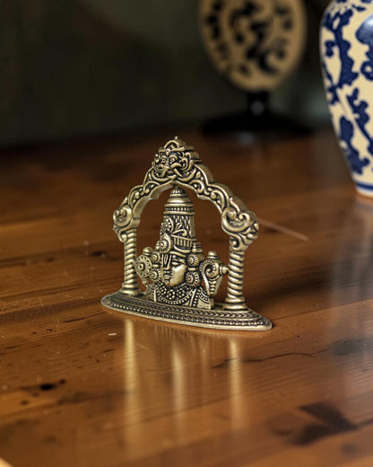 Rigvedaa brass Tirupati Balaji face murti with ornate crown and detailed ornaments, set within an arched frame.