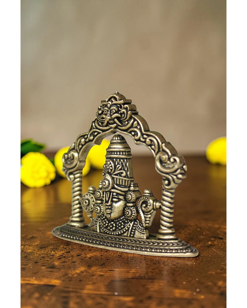 Rigvedaa brass Tirupati Balaji face murti with ornate crown and detailed ornaments, set within an arched frame.