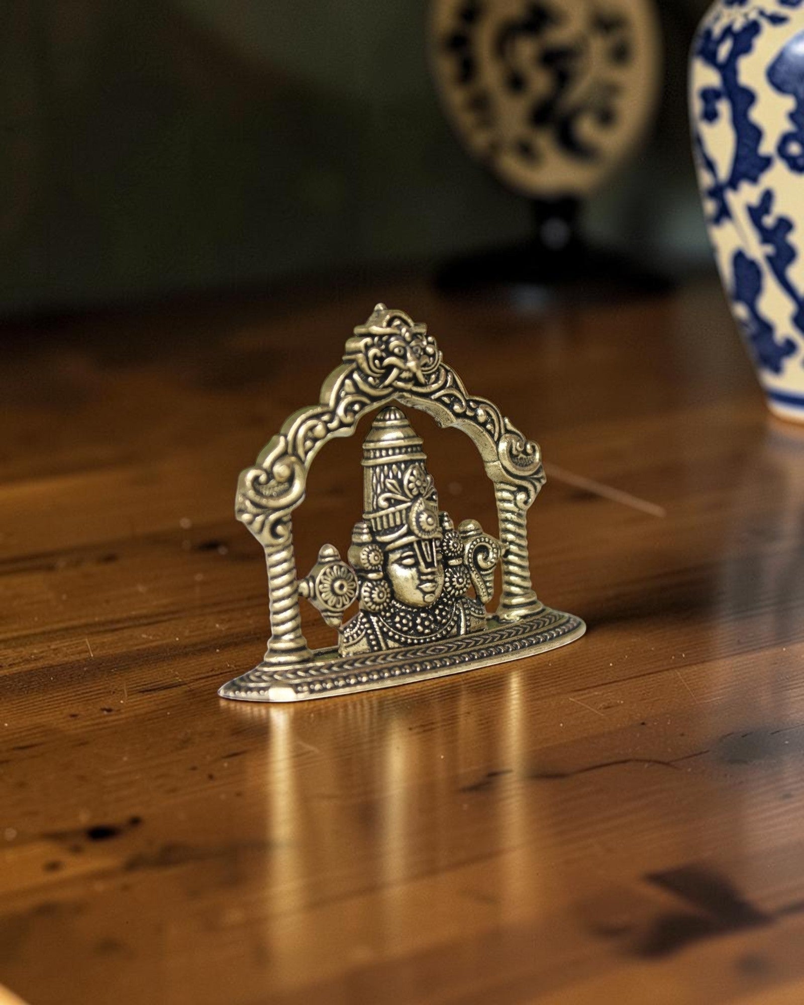 Rigvedaa brass Tirupati Balaji face murti with ornate crown and detailed ornaments, set within an arched frame.