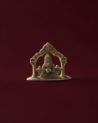 Rigvedaa™ brass Lord Venkateswara Tirupati Balaji face idol with intricate crown detailing on a dark red background.