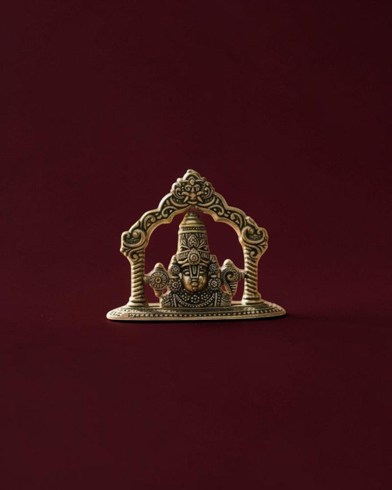 Rigvedaa™ brass Lord Venkateswara Tirupati Balaji face idol with intricate crown detailing on a dark red background.