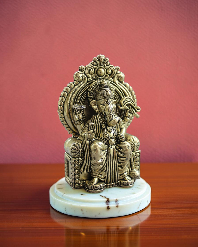 Rigvedaa™ Ornate antique brass Ganesha statue seated on an elaborate throne, detailed carvings, spiritual decor.