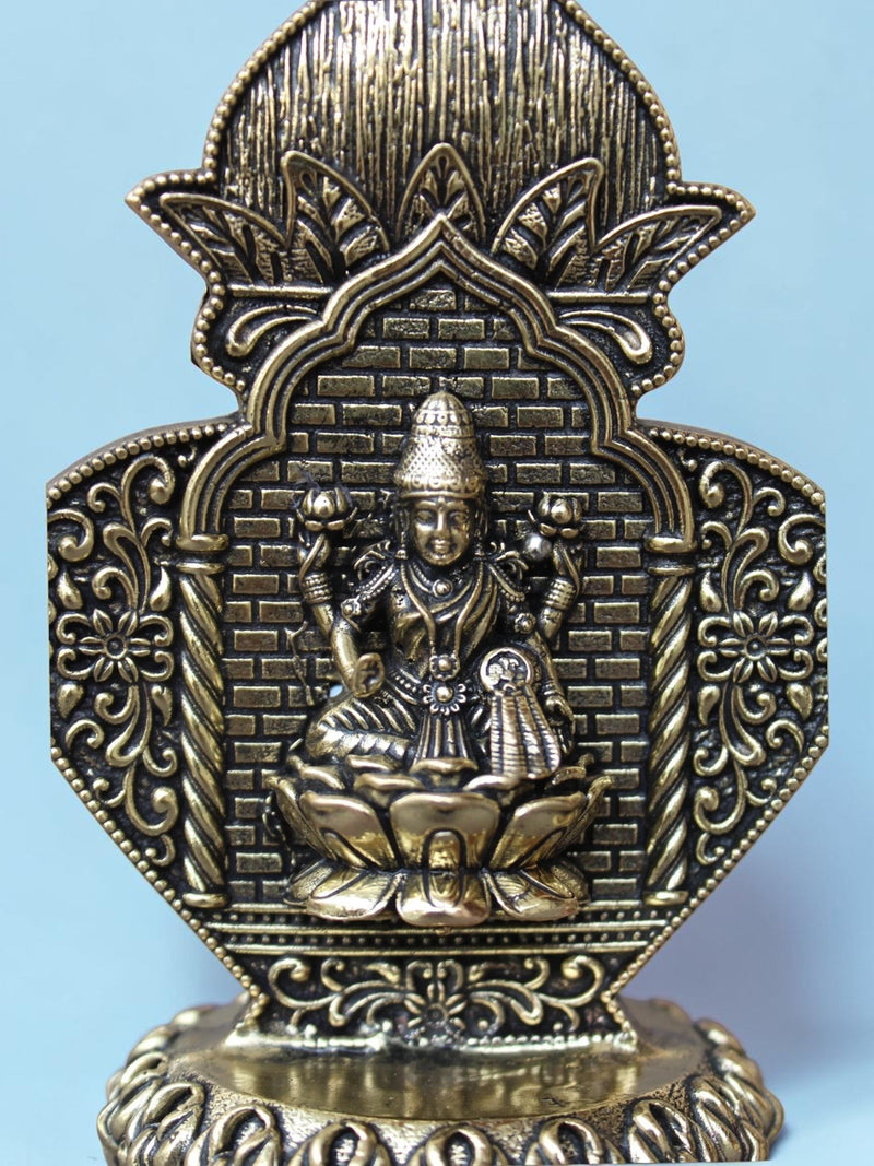 Rigvedaa™ Lakshmi idol in antique gold finish with ornate arch frame, floral motifs, and lotus pedestal base.