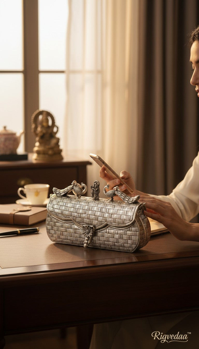 Rigvedaa™ Leela silver plated brass clutch with intricate carvings and decorative animal figures. Features a woven texture and ornate clasp.
