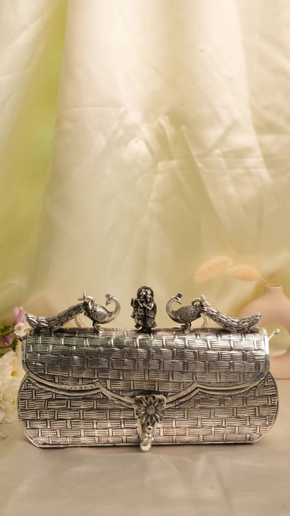 Rigvedaa™ Leela silver plated brass clutch with intricate carvings of peacocks and Radha Krishna figures.