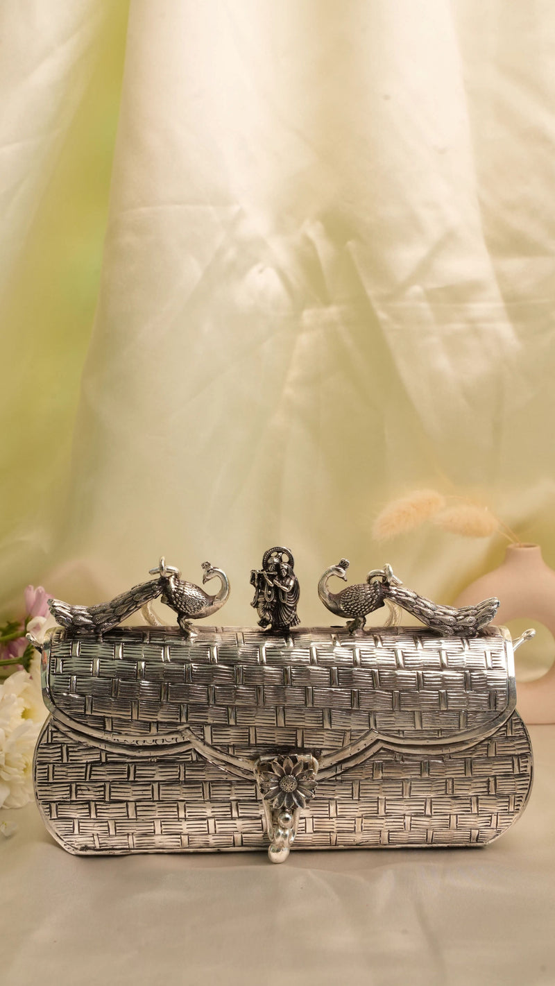 Rigvedaa™ Leela silver plated brass clutch with intricate carvings of peacocks and Radha Krishna figures.