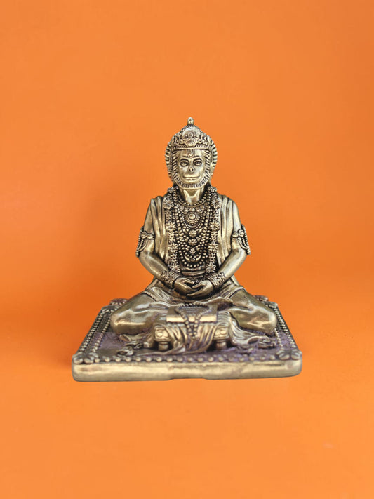 Rigvedaa™ Lord Hanuman meditating brass statue in a serene seated posture with intricate jewelry on orange background