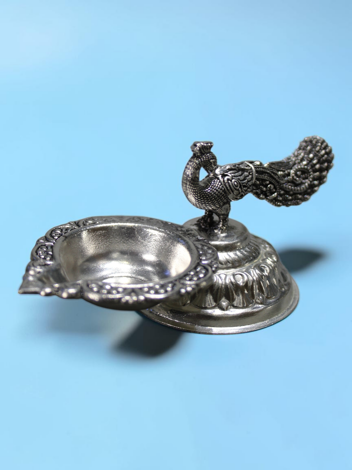 Rigvedaa™ silver plated brass peacock diya oil lamp with an intricate tail design and lotus pedestal base.
