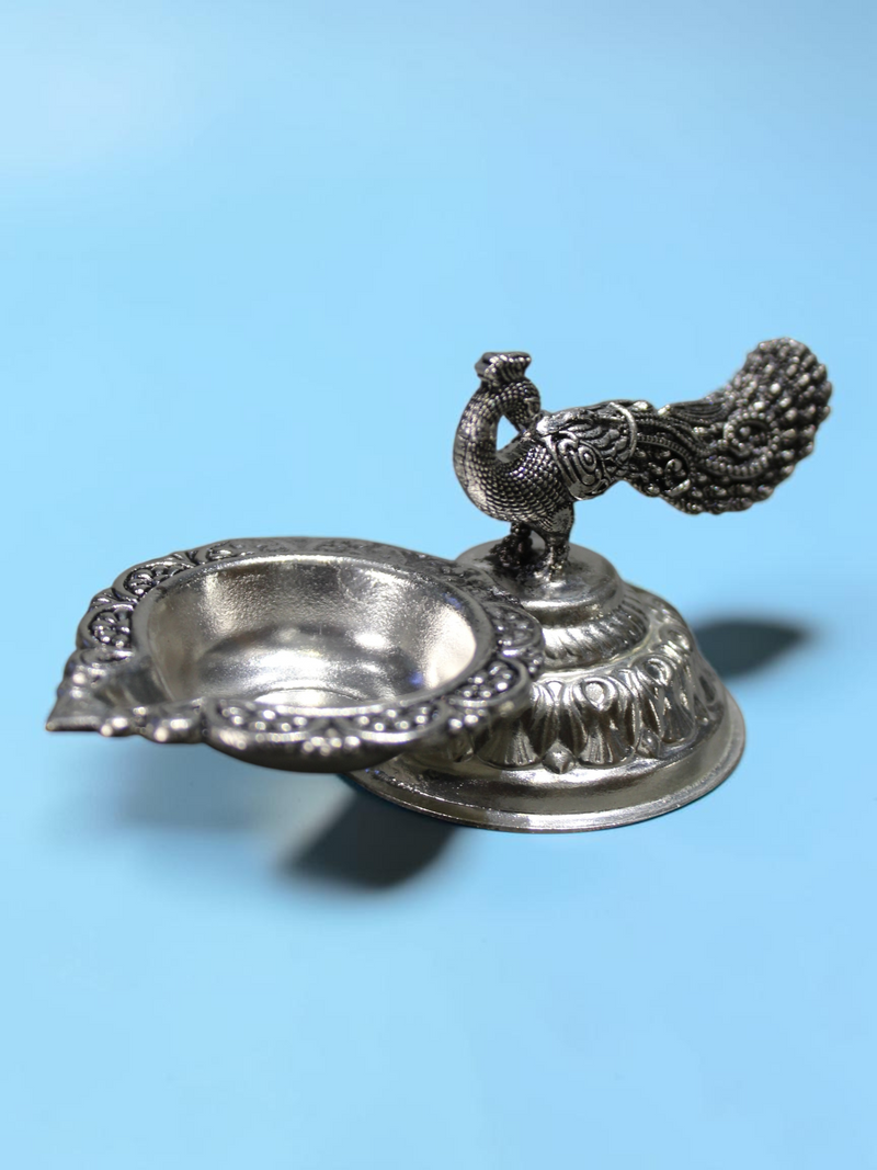 Rigvedaa™ silver plated brass peacock diya oil lamp with an intricate tail design and lotus pedestal base.