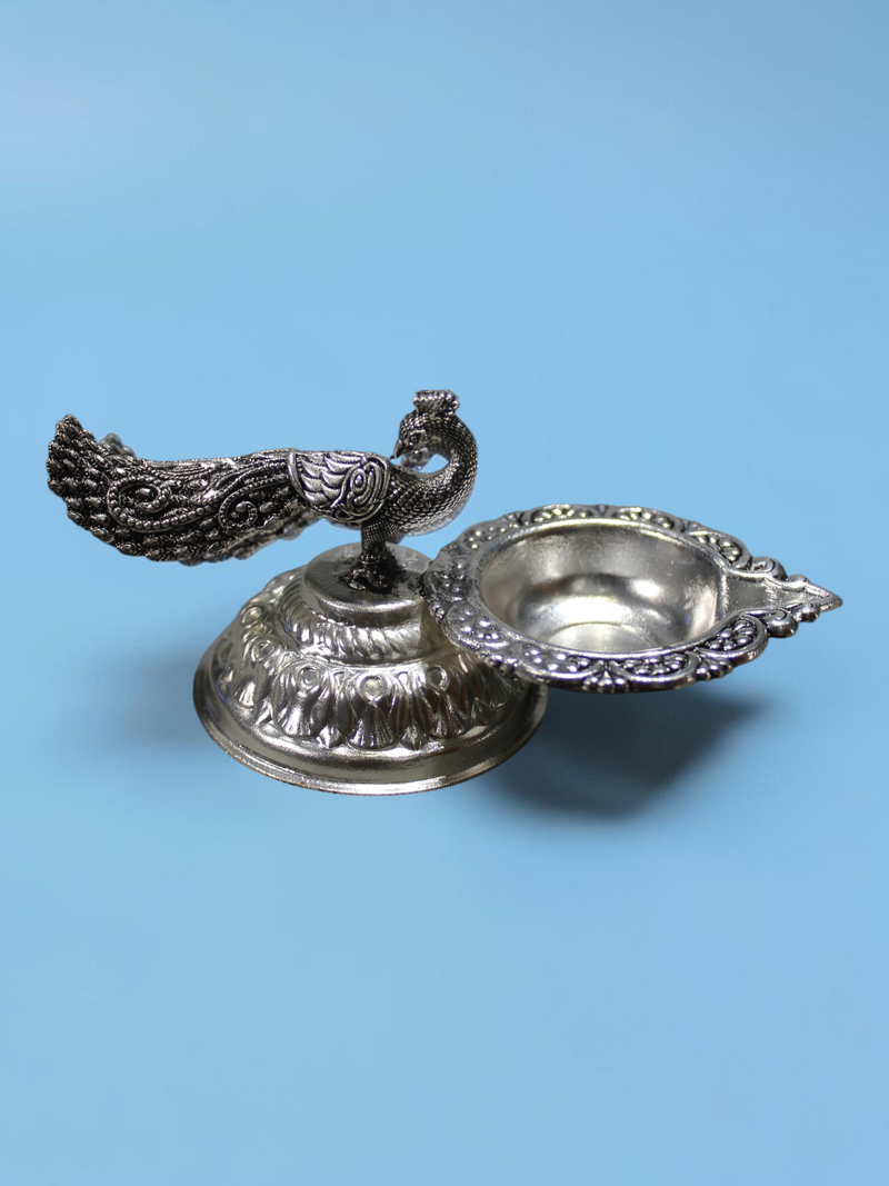 Rigvedaa™ silver plated brass peacock diya oil lamp with a detailed tail and lotus-inspired pedestal base.