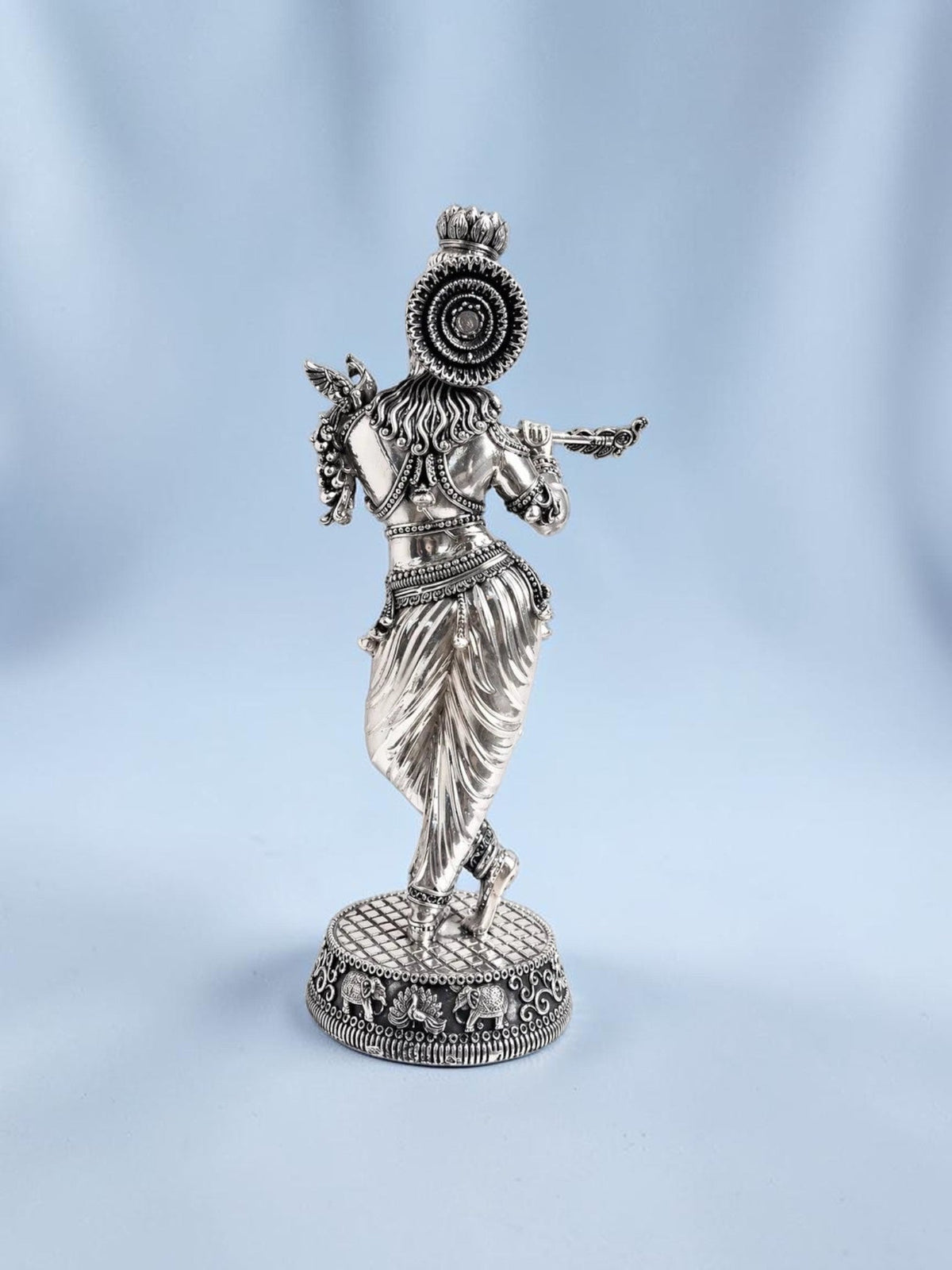 Rear view of an 18-inch Rigvedaa™ silver-plated brass Krishna statue in tribhanga posture playing a flute.