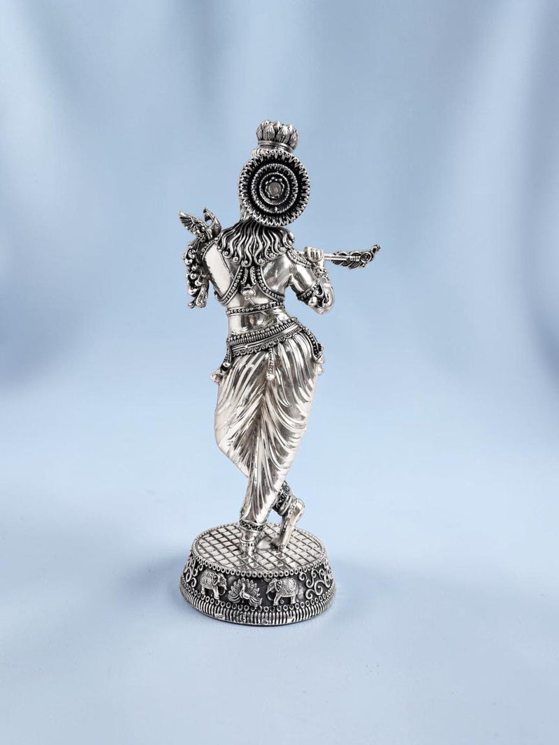 Rear view of an 18-inch Rigvedaa™ silver-plated brass Krishna statue in tribhanga posture playing a flute.