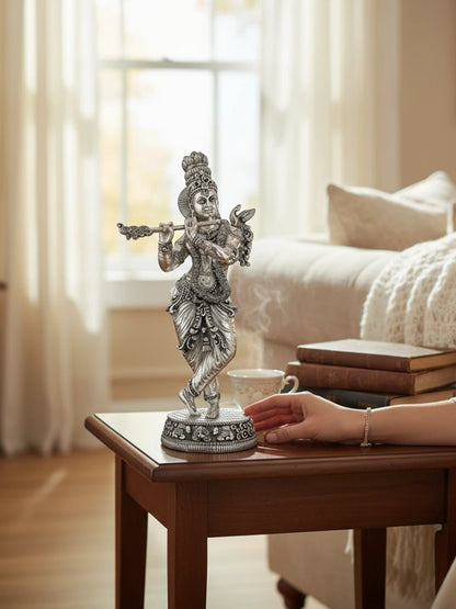 Rigvedaa™ 18-inch silver-plated brass Krishna statue in Tribhanga pose playing a flute on a wooden side table.