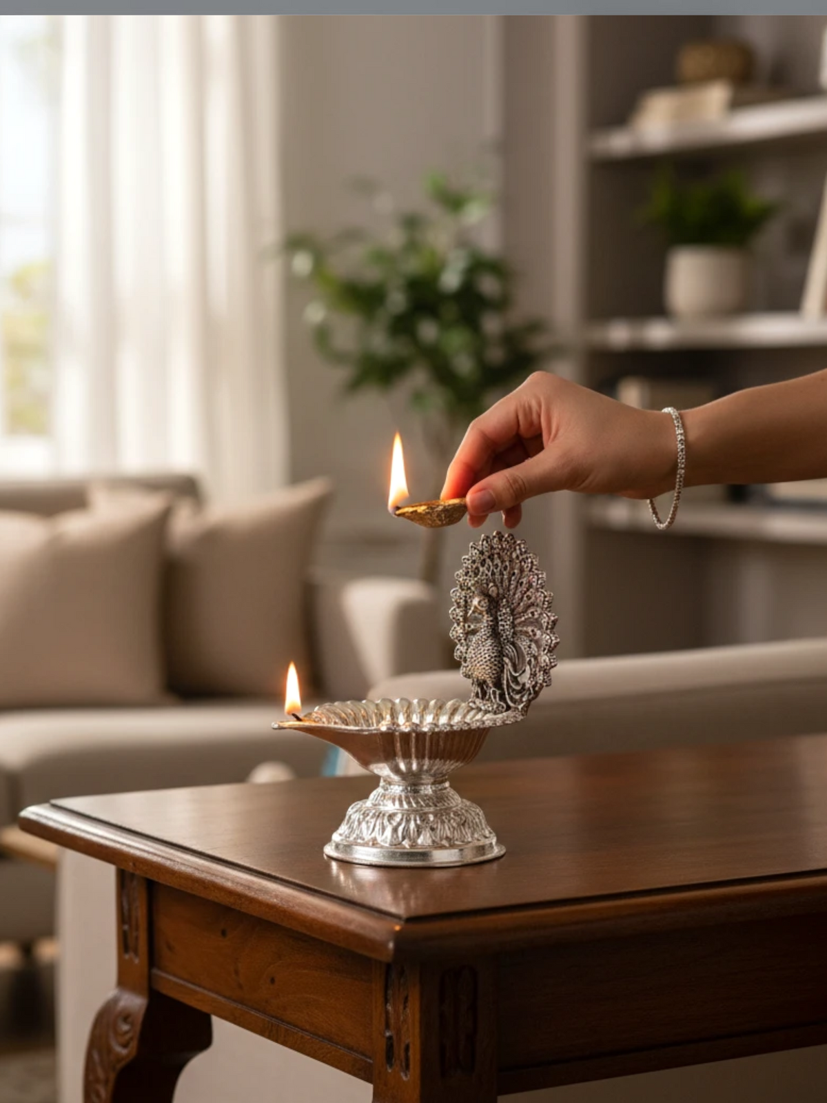 Rigvedaa™ silver plated brass peacock diya oil lamp with lotus bowl design being lit on a wooden table in a home.