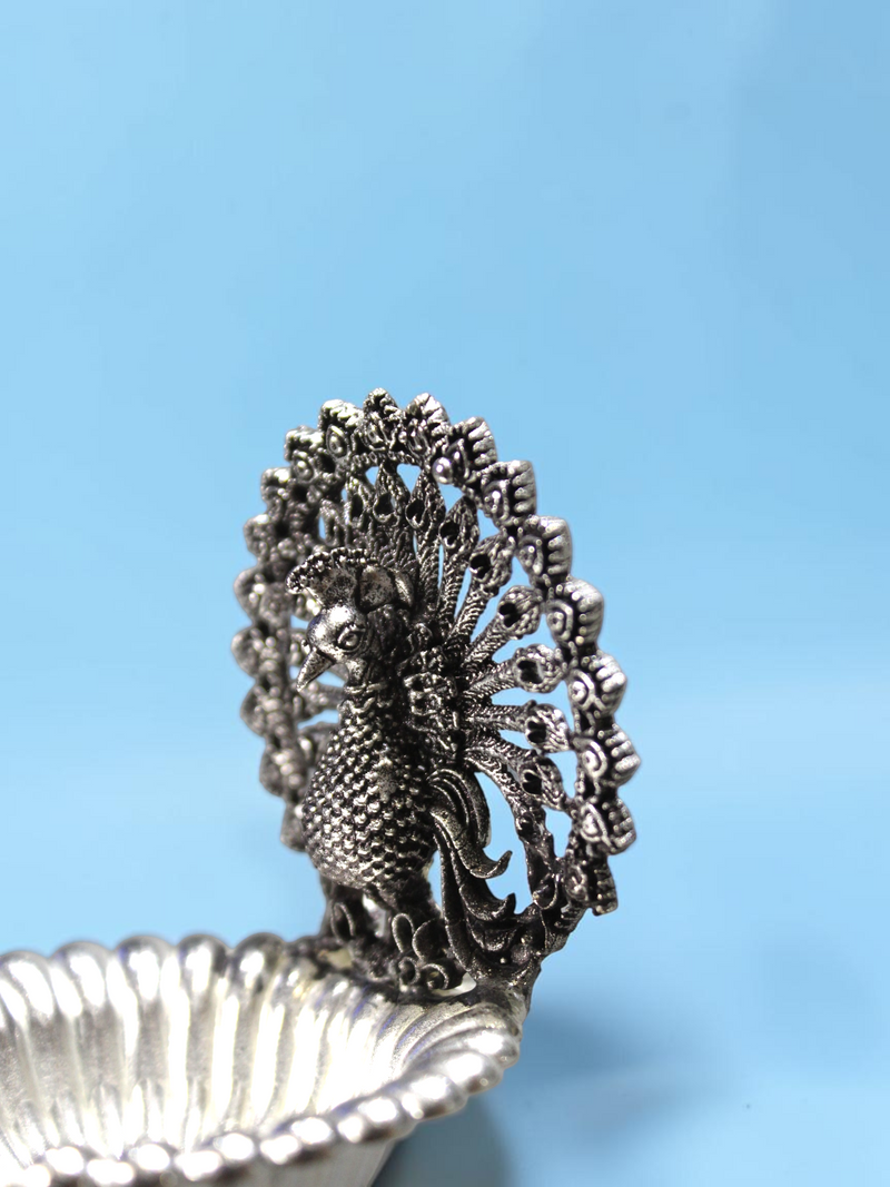 Rigvedaa™ silver plated brass peacock diya with intricate lotus petal bowl and detailed open-feather peacock design.