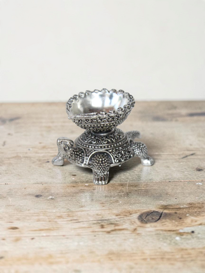 Rigvedaa™ silver-toned turtle diya oil lamp holder with intricate traditional metal detailing for home decor