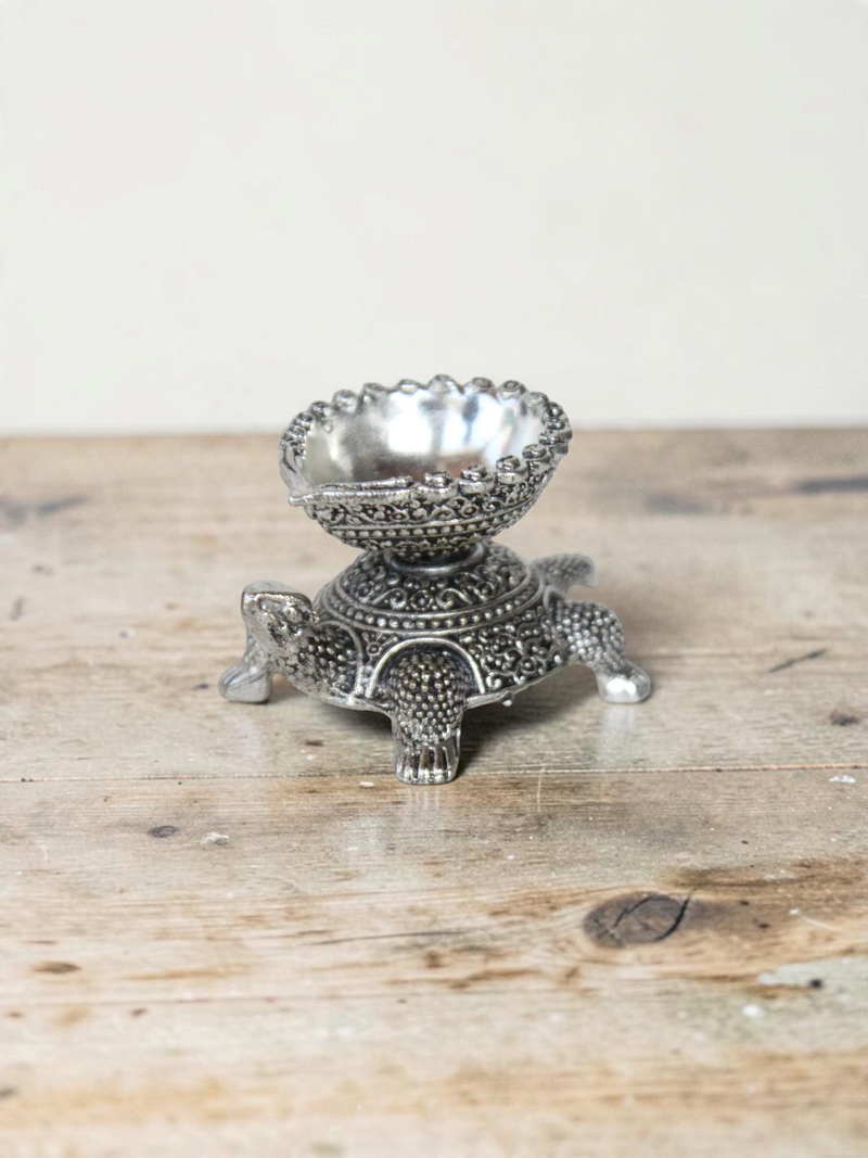 Rigvedaa™ silver-toned turtle diya oil lamp holder with intricate traditional metal detailing for home decor