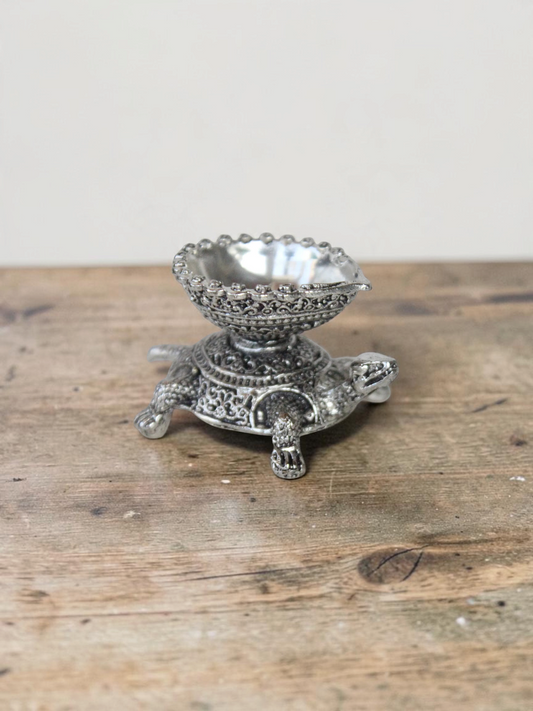 Rigvedaa™ silver-toned turtle diya oil lamp holder with intricate traditional metalwork for home decor and prayer.